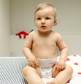 Bébé assis sur une table à langer sur un lange marinière et cœurs rouges en couches Carryboo 