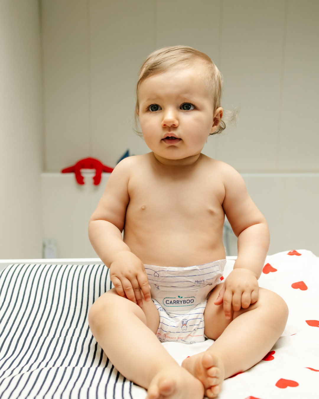 Bébé assis sur une table à langer sur un lange marinière et cœurs rouges en couches Carryboo 